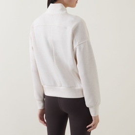 Model wearing Spanx Sweat Top in Oatmeal Heather, rear view, half-zip style with ribbed cuffs and hem, styled with dark leggings.