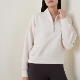 Model wearing Spanx Sweat Top in Oatmeal Heather, silver half-zip, ribbed cuffs and hem, styled with dark leggings.