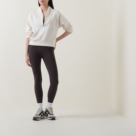 Model wearing Spanx Oatmeal Heather sweat top with half-zip neck, styled with dark leggings, white socks and grey trainers.