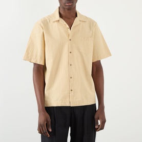 Model wearing A.P.C. Jude Pocket Shirt in beige with bowling collar, short sleeves, and chest pocket, styled with black trousers
