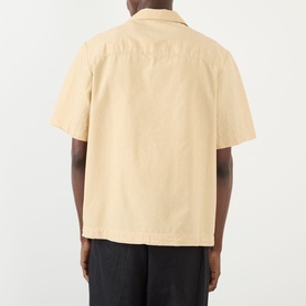 Model wearing A.P.C. Jude Pocket Shirt in beige, rear view, short sleeves and straight hemline, styled with black trousers