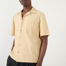 Model wearing A.P.C. Jude Pocket Shirt in beige with bowling collar, short sleeves, and chest pocket, styled with dark trousers