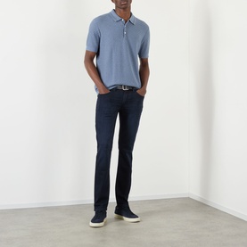 Model wearing Paige Lennox Slim-Leg Jeans in Hastings dark wash, styled with a blue polo shirt and white trainers.