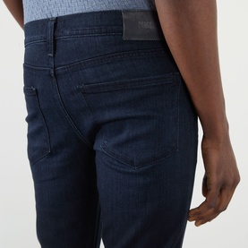 Model wearing Paige Lennox Slim-Leg Jeans in Hastings, dark-wash indigo denim, showing rear five-pocket detail and tonal stitching.