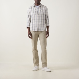 Model wearing Seven Jeans Slimmy Stretch Slim Leg Jeans in Rawhide, styled with a white check shirt and white trainers.