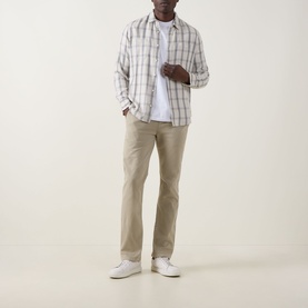 Model wearing Seven Jeans Slimmy Stretch Slim Leg Jeans in Rawhide, styled with a plaid overshirt, white tee and white trainers.