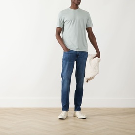 Model wearing Seven Jeans Dusty Blue Crew Neck T, styled with mid-blue jeans and white trainers, holding a cream tote bag.