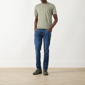 Model wearing Seven Jeans Army Crew Neck T-Shirt in sage green, styled with mid-blue slim jeans and grey trainers.