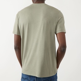 Model wearing Seven Jeans Army Crew Neck T-shirt in sage green lyocell-cotton blend, rear view, paired with blue jeans.