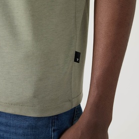 Model wearing Seven Jeans Army Crew Neck T-shirt in sage green lyocell-cotton blend, styled with blue denim jeans. Small branded tab detail at hem.