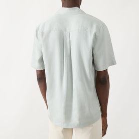 Model wearing Seven Jeans Dusty Blue Reg Shirt in lyocell, back view showing pleat detail and short sleeves, styled with cream trousers