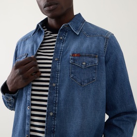 Model wearing Seven Jeans Western Denim Shirt in Canyon mid wash with tobacco stitching and snap placket, styled over a stripe tee.