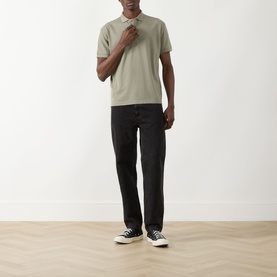 Model wearing Seven Jeans Army Regular Polo in sage green piqu&eacute;, styled with black straight-leg jeans and black high-top trainers.