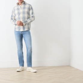 Model wearing Seven Jeans Haven slim jeans in light blue wash, styled with a white plaid shirt and cream trainers.