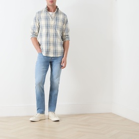 Model wearing Seven Jeans Haven slim jeans in light blue wash, styled with a pale plaid shirt and white trainers.