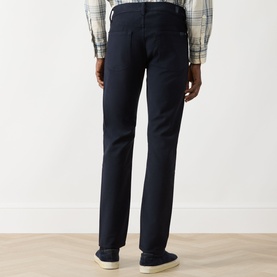 Model wearing Seven Jeans 3049 Slim Jeans in Ultramarine, rear view, styled with a plaid shirt and navy trainers.