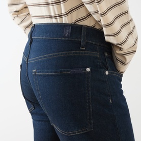 Model wearing Seven Jeans Sundown straight jeans in dark indigo denim, styled with a striped cream top. Close-up of back pocket detail.