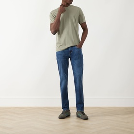 Model wearing Seven Jeans Slimmy Mid-Rise Tapered Jeans in Signal blue with a sage green T-shirt and grey trainers.