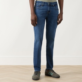 Model wearing Seven Jeans Slimmy Mid-Rise Tapered Jeans in Signal blue with whiskering and faded details, styled with grey trainers.