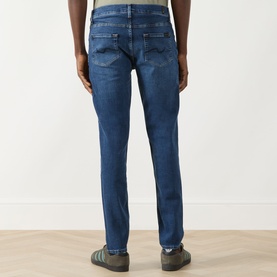 Model wearing Seven Jeans Slimmy Mid-Rise Tapered Jeans in Signal blue, back view showing five-pocket style and embroidered back pocket detail.