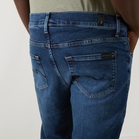 Model wearing Seven Jeans Slimmy Mid-Rise Tapered Jeans in Signal blue, showing rear five-pocket detail with embroidered back pocket and zip