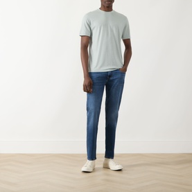 Model wearing Seven Jeans Slimmy Mid-Rise Tapered Jeans in Signal blue with a light grey t-shirt and white trainers.