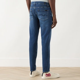 Model wearing Seven Jeans Slimmy Mid-Rise Tapered Jeans in Signal blue, back view, styled with white Comme des Gar&ccedil;ons trainers