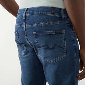 Model wearing Seven Jeans Slimmy Mid-Rise Tapered Jeans in Signal blue, showing rear five-pocket detail with embroidered back pocket and logo tab.