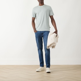 Model wearing Seven Jeans Slimmy Mid-Rise Tapered Jeans in Signal blue with a mint crew-neck tee and white trainers, holding a cream jacket.