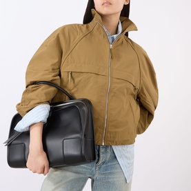 Model carrying Loewe Amazonia 180 Mini Top Handle Bag in black calfskin with silver-tone hardware, boxy silhouette; styled with tan bomber jacket and