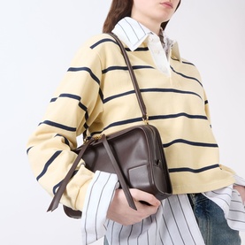 Model carrying Loewe Amazona 180 Small Top Handle Bag in Dark Chestnut, grained leather with gold-tone hardware, worn crossbody with striped top.