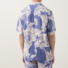 Model wearing OAS Mystea Rocco Printed Shirt in blue, rear view, with short sleeves and all-over tiger jungle print, styled with matching trousers.