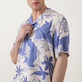 Model wearing OAS Mystea Rocco Printed Shirt in blue, short-sleeve viscose with notched collar and tropical print, hand raised to collar.
