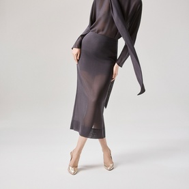 Model wearing Christian Louboutin heels in Platine/Lin Platine, styled with a dark grey midi skirt and sheer long-sleeve top.