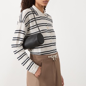 Model carrying MMK Izzy Small Pebbled Leather Barrel Pochette in black with silver-tone hardware, worn crossbody over striped knit top