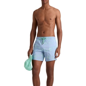 Model wearing Vilebrequin swim shorts in Cloudy blue with drawstring waist, holding a matching green wash bag.