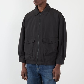 Model wearing Edwin Chaos Water-Resistant Jacket in black with flat collar, zip fastening, flap patch pockets, and elasticated hem. Styled with blue