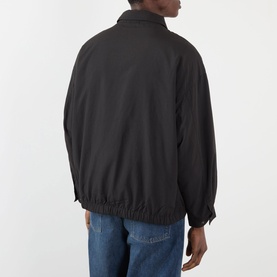 Model wearing Edwin Chaos Water-Resistant Jacket in black, rear view, showing elasticated hemline and tab-adjustable cuffs, styled with blue jeans.