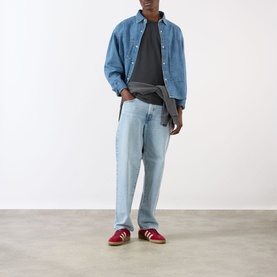 Model wearing Edwin Axiom Logo T-Shirt in dark grey, styled with light blue denim shirt, jeans, and red trainers.