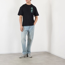 Model wearing Edwin Hardware Store Logo T-Shirt in black with chest graphic, styled with light-wash jeans and grey trainers.
