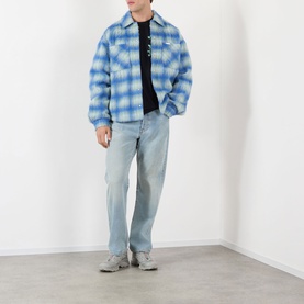 Model wearing Edwin Hardware Store Logo T-Shirt in black, styled with blue check overshirt and light wash jeans.