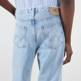 Model wearing Edwin Loose Straight Leg Jeans in light used blue, rear view showing logo badge, five-pocket style and faded denim detailing.