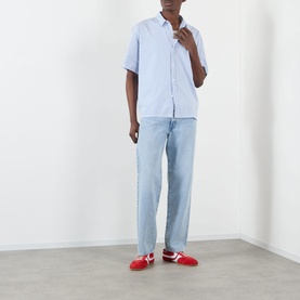 Model wearing Edwin Toledo Stripe Shirt in blue with short sleeves, paired with light wash jeans and red trainers.