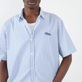 Model wearing Edwin Toledo Stripe Shirt in blue and white stripe, short sleeves, classic collar, embroidered logo on chest, styled over white tee.