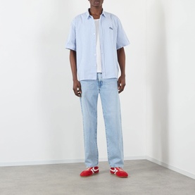 Model wearing Edwin Toledo Stripe Shirt in blue, short sleeves, classic collar, styled with light wash jeans and red trainers.