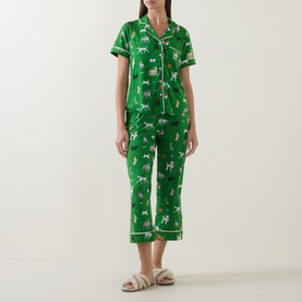 Model wearing Kate Spade Dog Park green pyjamas with all-over dog print, short-sleeve shirt and cropped trousers, styled with fluffy sliders