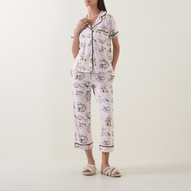 Model wearing Kate Spade City Stroll pyjamas in white with illustrated print, short-sleeve button-up top and cropped trousers, styled with fluffy