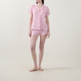 Model wearing Stripe & Stare Cherry Short Pyjama Set in Cherry Baby; pink cherry-print shorts and short-sleeve shirt with notched lapels and piped