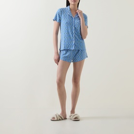 Model wearing Stripe & Stare Sorento Lemon pyjamas; short-sleeve shirt and shorts in blue ditsy print, styled with fluffy white sliders.