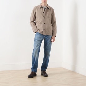 Model wearing Nudie Jeans Barney Worker Overshirt in Mud, styled with blue jeans and brown leather shoes.